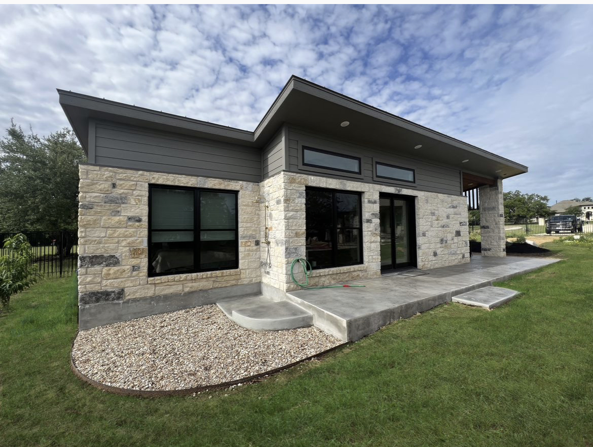Custom casita and pool house with stone and dark siding, large windows and a covered patio