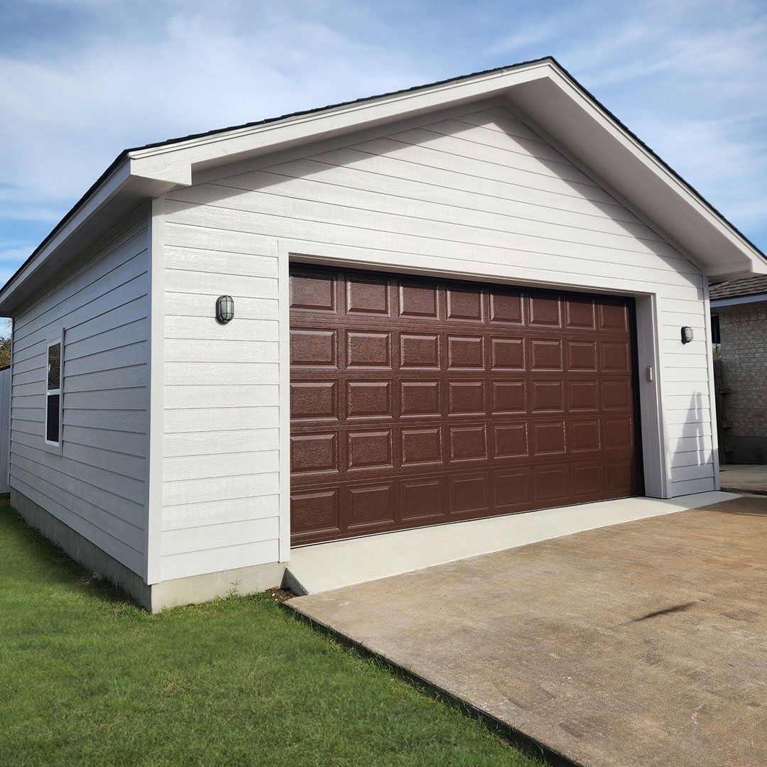 Detached garage with a white exterior and brown carriage-style door