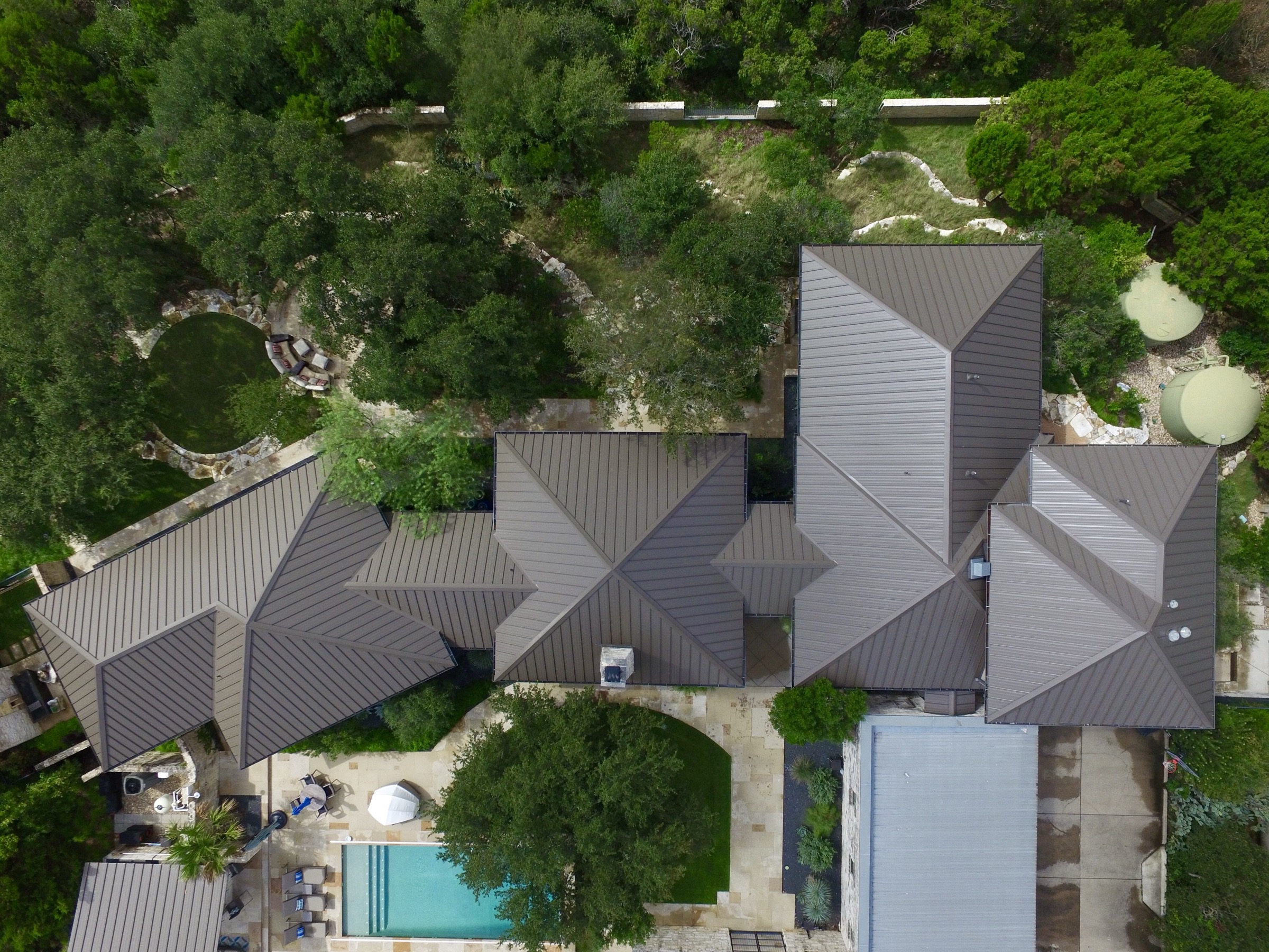Overhead aerial view of a residential standing-seam metal roof estate with a pool