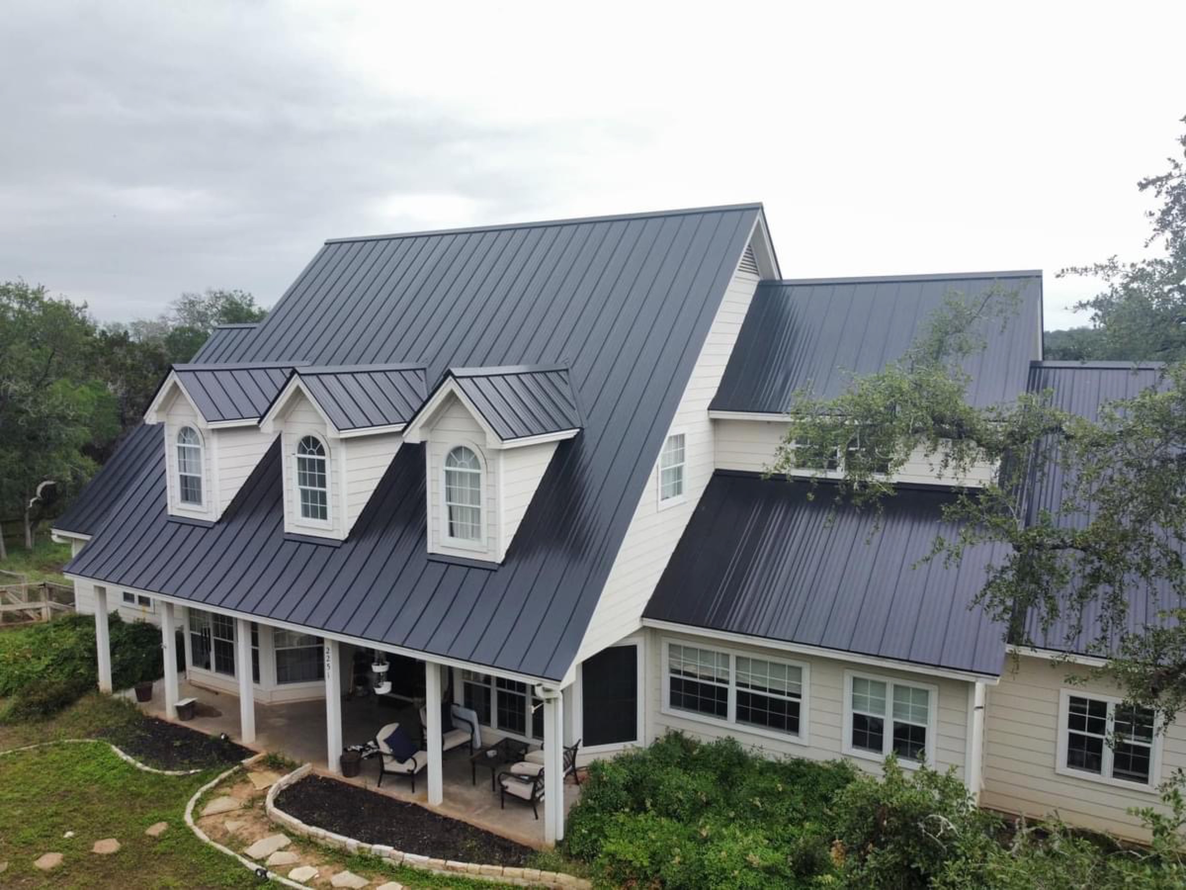 Aerial view of a white Central Texas home with a dark standing-seam metal roof