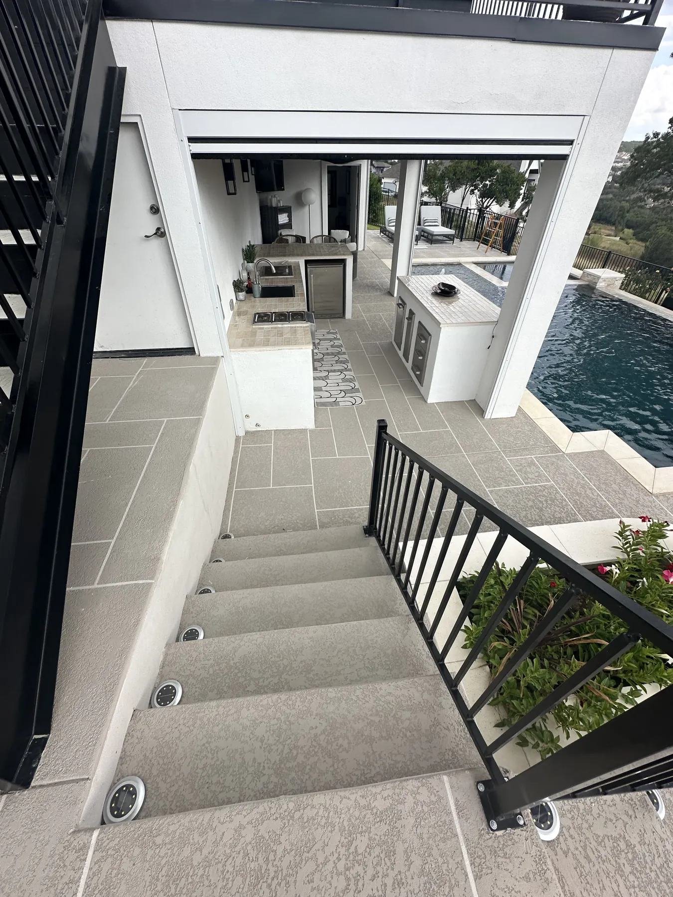 Finished tiled terrace with stairs and a covered outdoor kitchen beside the pool