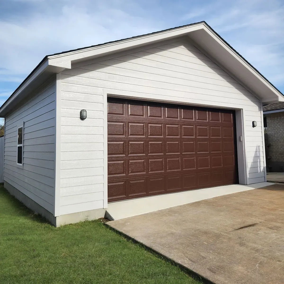 Custom detached garage with white board-and-batten siding and a brown overhead door